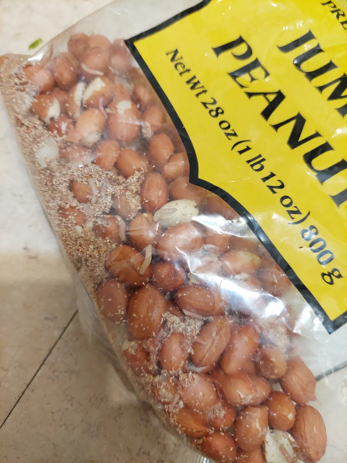 Clear plastic bag of red-skinned peanuts with small pale larvae and a sprinkling of light brown, crumbly droppings among the nuts